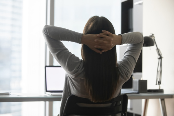 Woman at desk with a laptop, relaxing with her hands behind her head