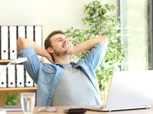 Relaxed entrepreneur sitting in a chair with his arms behinds behind his head, in an office