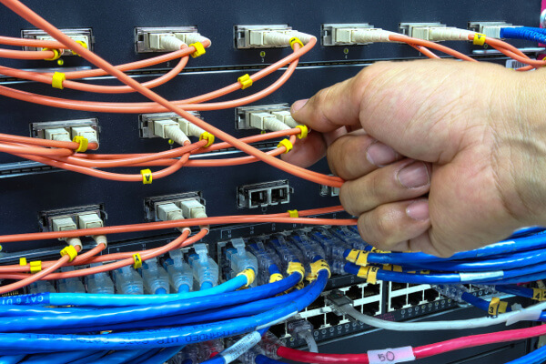 Technician connecting fiber network to switch port in a server room