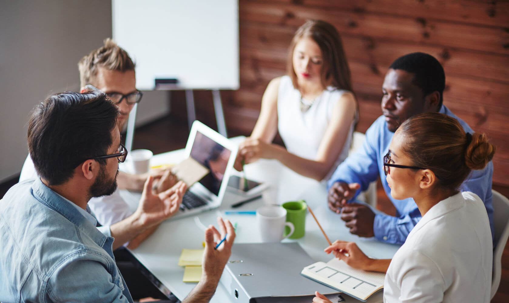 Group of young professionals conversing around a table with a laptop and coffee mugs