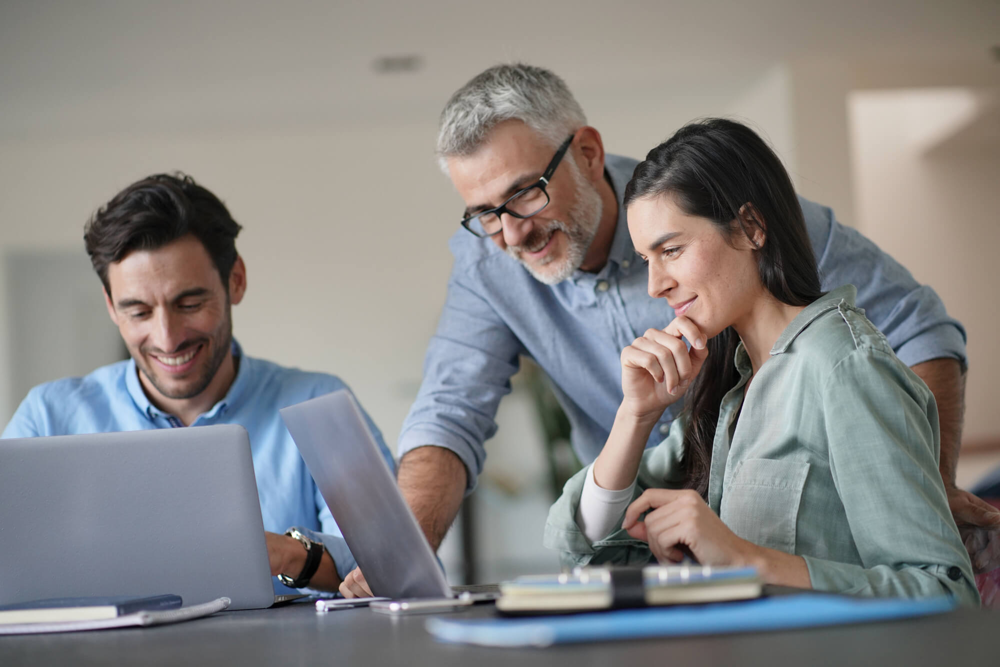 Older professional looking over younger employees work on their laptops