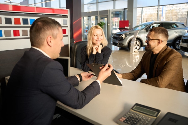 Three people sitting at a table in a dealership