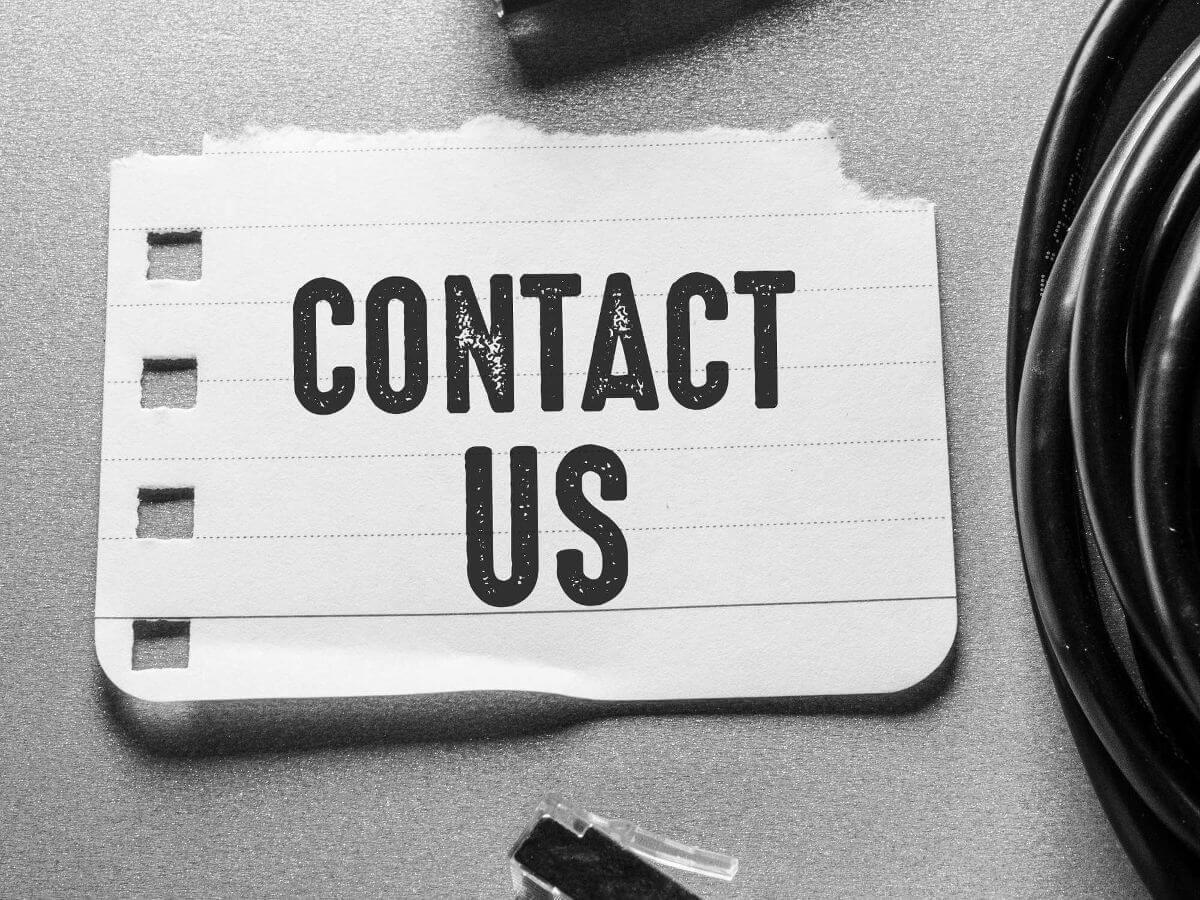 'Contact Us' in block letters on a torn off portion of paper with square holes down the side